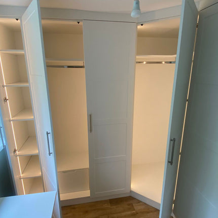 Open wardrobe with 4mm 3000K warm white COB LED strip lights integrated within micro recessed profile. 24V. Inside a bedroom with wooden flooring and a window.