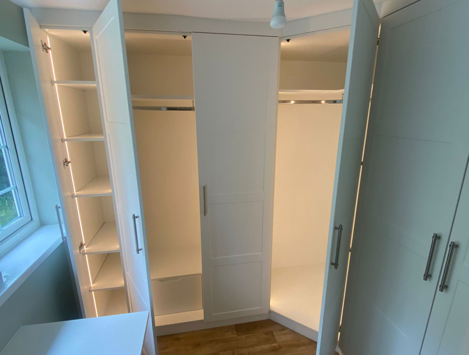 Open wardrobe with 4mm 3000K warm white COB LED strip lights integrated within micro recessed profile. 24V. Inside a bedroom with wooden flooring and a window.