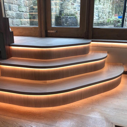 Integrated 3000K warm white 4mm COB LED strip lights within curved wooden steps. Providing a warm halo of light next to a window.