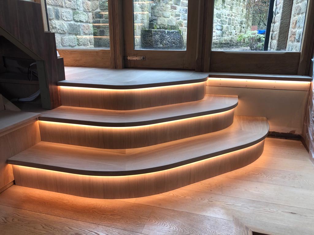 Integrated 3000K warm white 4mm COB LED strip lights within curved wooden steps. Providing a warm halo of light next to a window.