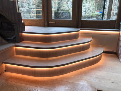 Integrated 3000K warm white 4mm COB LED strip lights within curved wooden steps. Providing a warm halo of light next to a window.