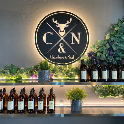 Bottles on an illuminated warm white shelf with a well lit 'Chambers & Neal' logo in the background. 24V 4mm COB LED strip lights within recessed silver micro profile used.