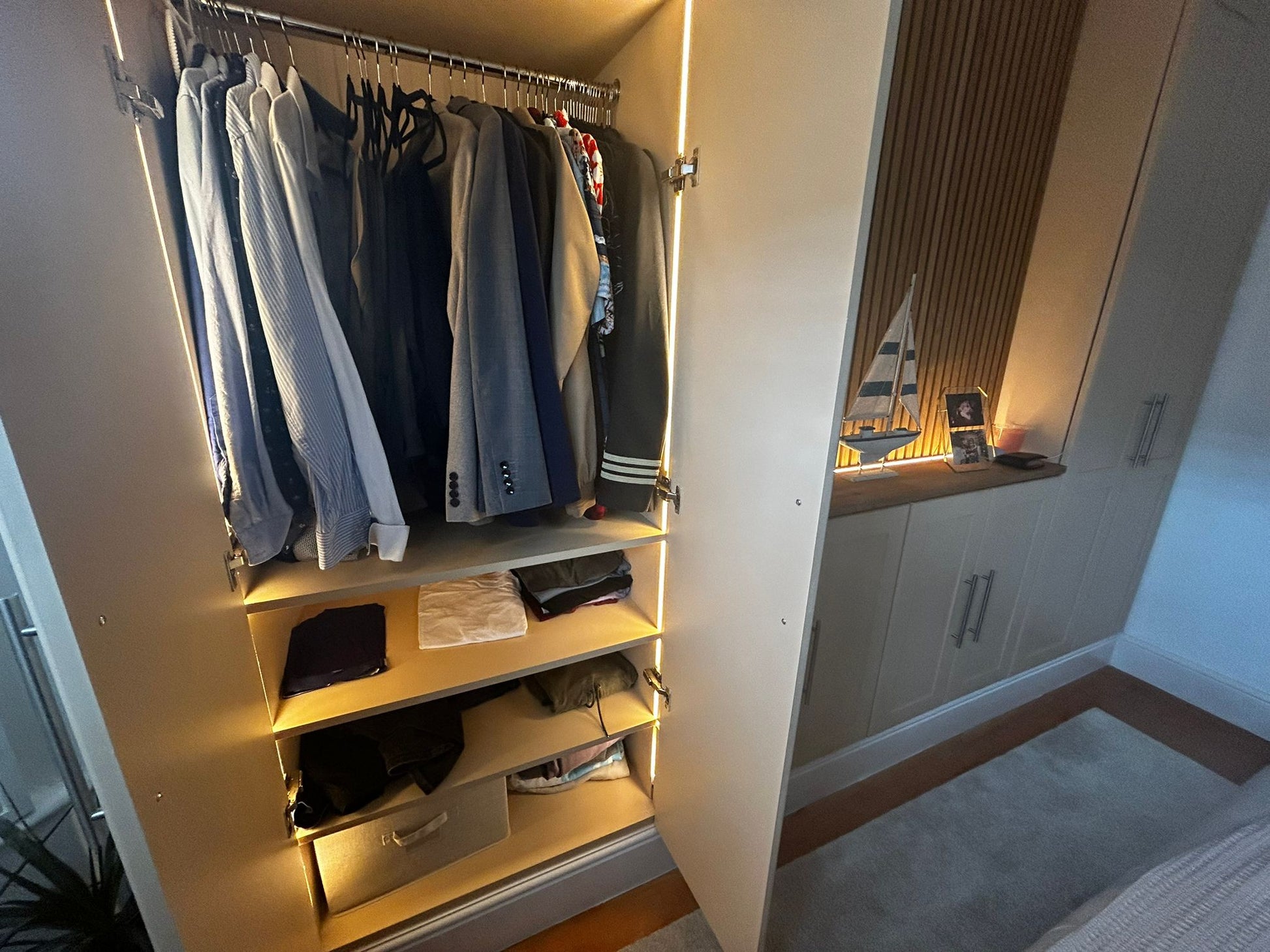 Open closet with hanging clothes and shelves, illuminated by warm 2700K integrated light lines. 4mm seamless COB LED strip lights used triggered on/off by 12V-24V double door sensors.